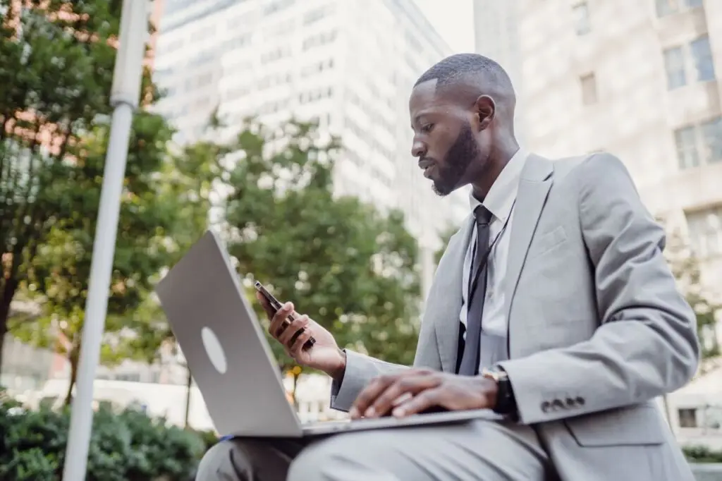 What Entrepreneurs Deal With Businessman in a suit using a laptop and smartphone in an urban setting, blending technology with business.