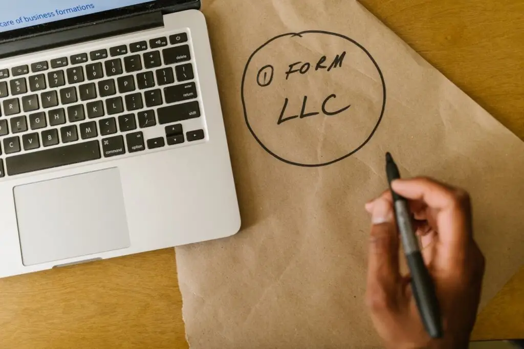Registering a Business Close-up of hand writing 'Form LLC' on craft paper beside a laptop, indicating business planning.